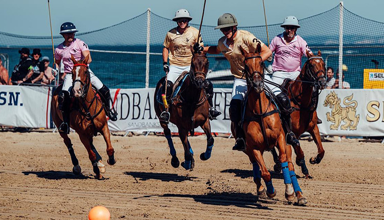 Men on horses playing polo on the sand.