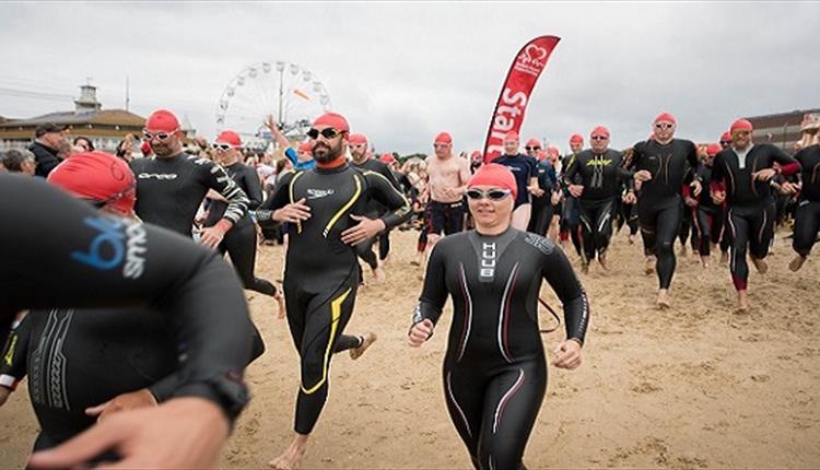 Swimmers in wetsuits running on the sand