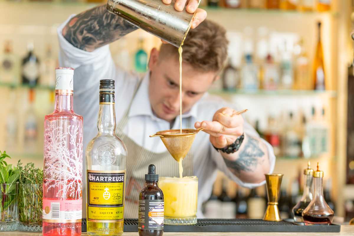 barman straining ingredients into cocktail glass